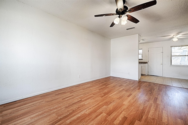 unfurnished living room featuring visible vents, light wood-style floors, a ceiling fan, a textured ceiling, and baseboards