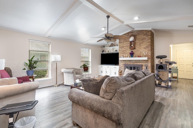 living area with ceiling fan, a fireplace, vaulted ceiling with beams, and wood finished floors