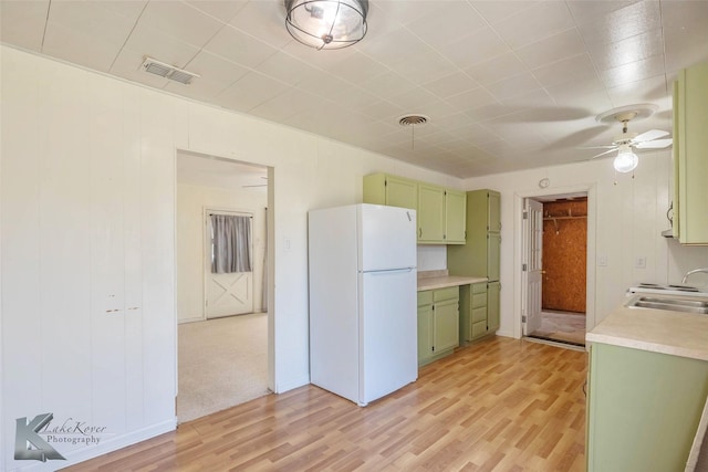 kitchen with light countertops, visible vents, green cabinets, freestanding refrigerator, and a sink