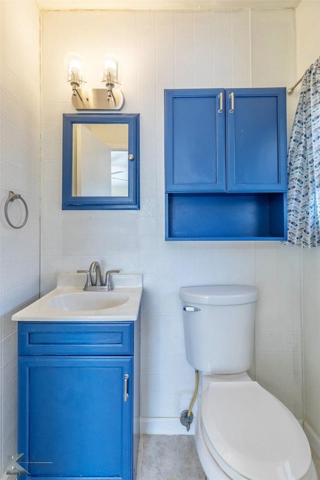 bathroom with toilet, tile patterned floors, vanity, and tile walls