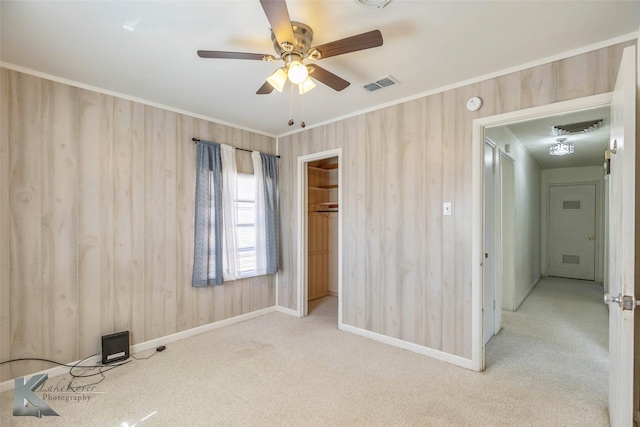 unfurnished bedroom with ornamental molding, carpet, a walk in closet, and visible vents