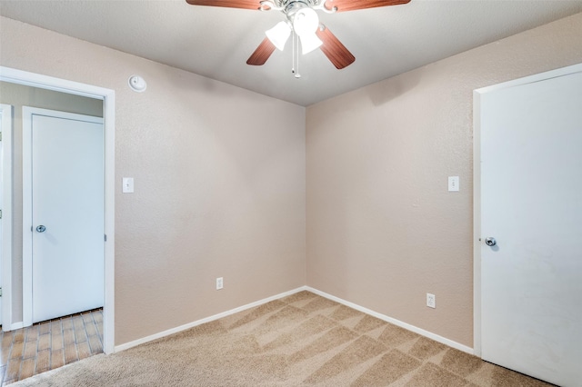 empty room featuring light carpet, ceiling fan, a textured wall, and baseboards