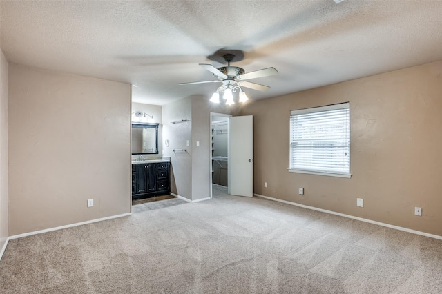 unfurnished bedroom featuring light carpet, baseboards, ensuite bath, a spacious closet, and a textured ceiling