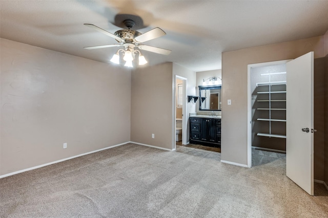 unfurnished living room with a ceiling fan, light colored carpet, a sink, and baseboards