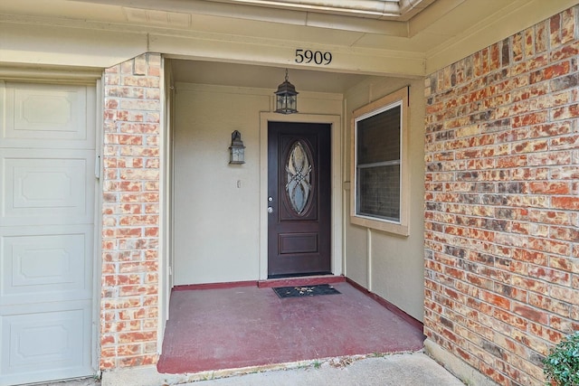 view of exterior entry featuring a garage, a porch, and brick siding