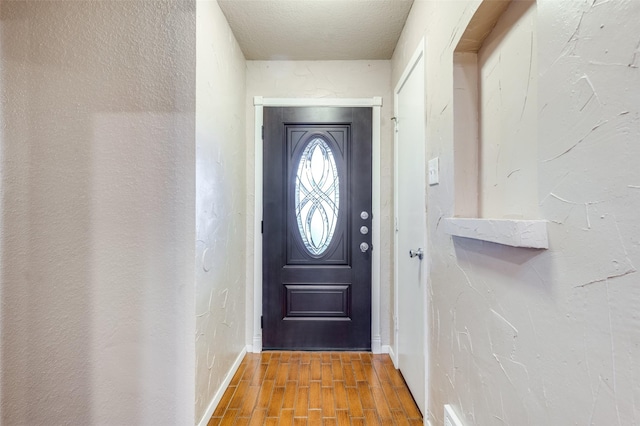 entryway featuring a textured ceiling, a textured wall, wood finished floors, and baseboards