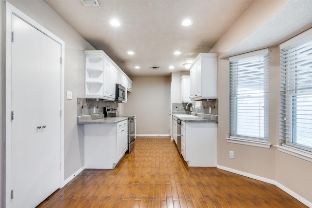 kitchen with open shelves, decorative backsplash, appliances with stainless steel finishes, white cabinetry, and baseboards