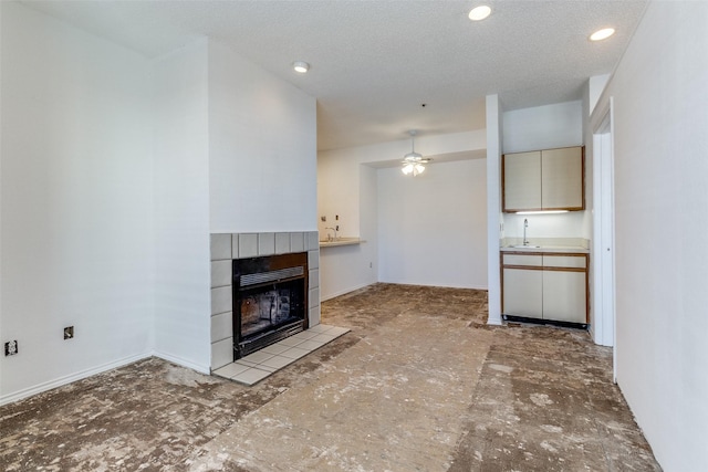 unfurnished living room featuring a ceiling fan, a tile fireplace, a textured ceiling, a sink, and recessed lighting