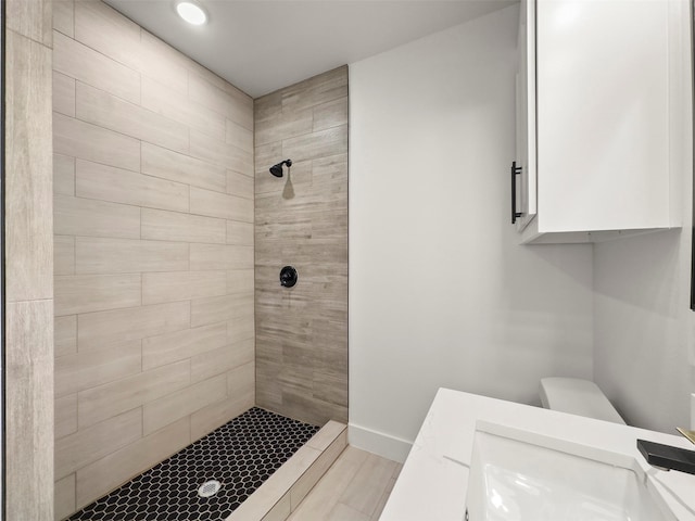 bathroom featuring toilet, a tile shower, and vanity