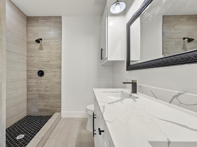 full bathroom with baseboards, a tile shower, vanity, and toilet