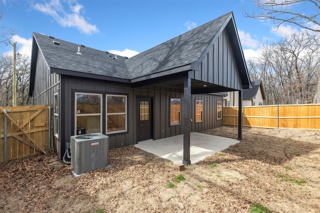 rear view of property with a shingled roof, board and batten siding, a patio area, central AC, and a fenced backyard