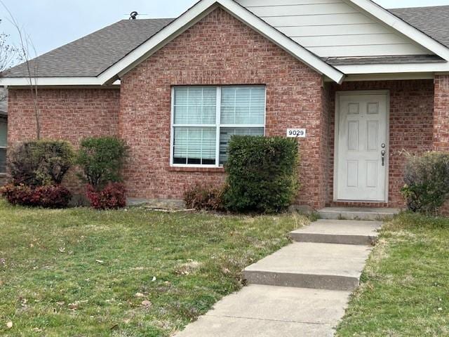 view of front of property with roof with shingles, a front lawn, and brick siding