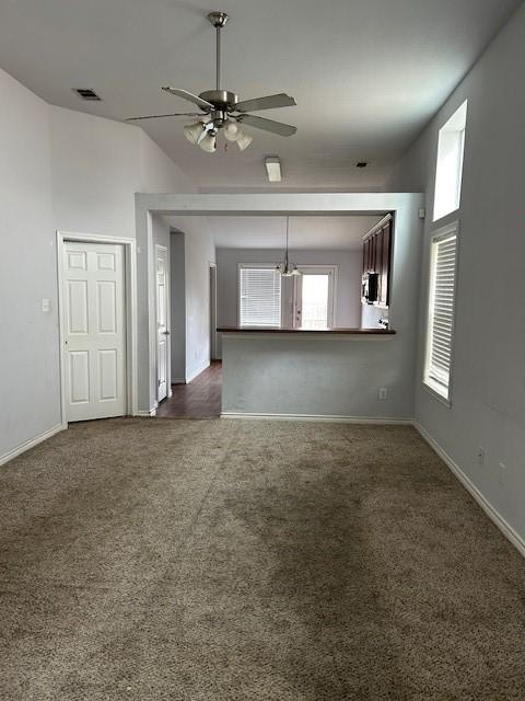 unfurnished living room with ceiling fan, dark colored carpet, visible vents, and baseboards