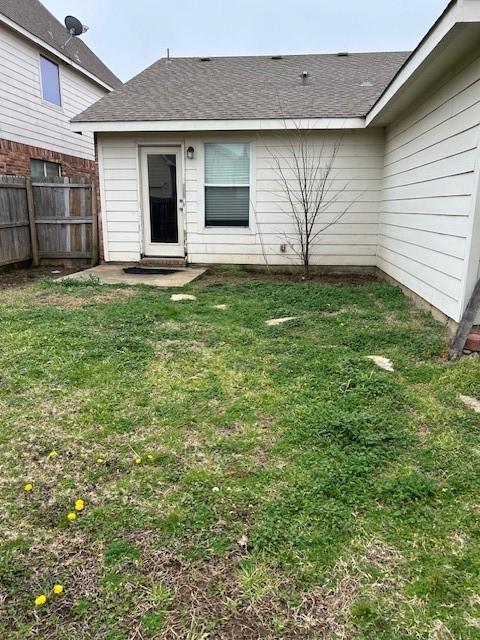 back of property with a yard, roof with shingles, and fence