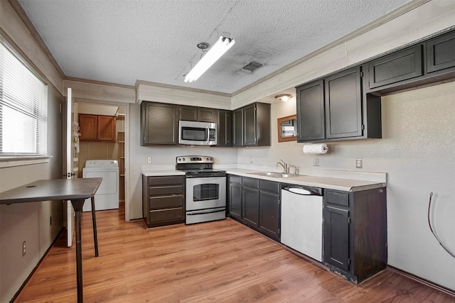 kitchen featuring light wood finished floors, washer / clothes dryer, appliances with stainless steel finishes, a sink, and a textured ceiling