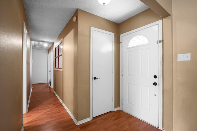 entryway with a textured ceiling, wood finished floors, and baseboards