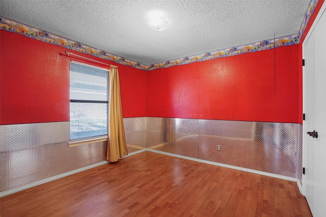 spare room with wood finished floors, a wainscoted wall, a textured ceiling, and wallpapered walls