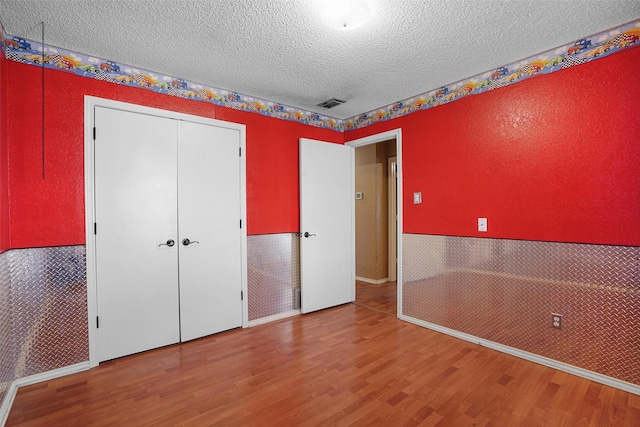 unfurnished bedroom with a textured ceiling, a textured wall, wood finished floors, visible vents, and a closet