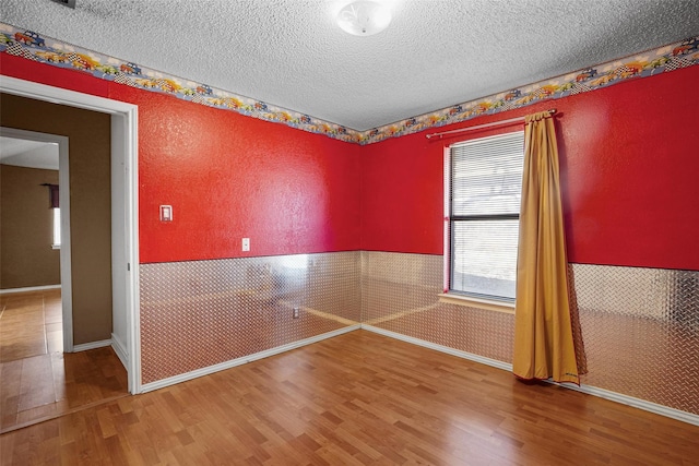 unfurnished room featuring a textured ceiling, a textured wall, a wainscoted wall, and wood finished floors