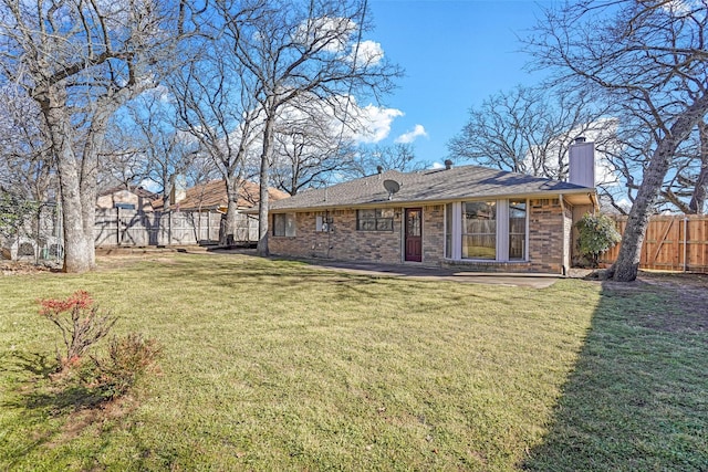 rear view of property with a yard, brick siding, fence, and a chimney