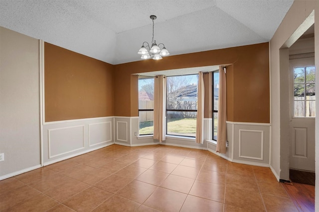 unfurnished dining area with vaulted ceiling, a textured ceiling, tile patterned flooring, and a chandelier