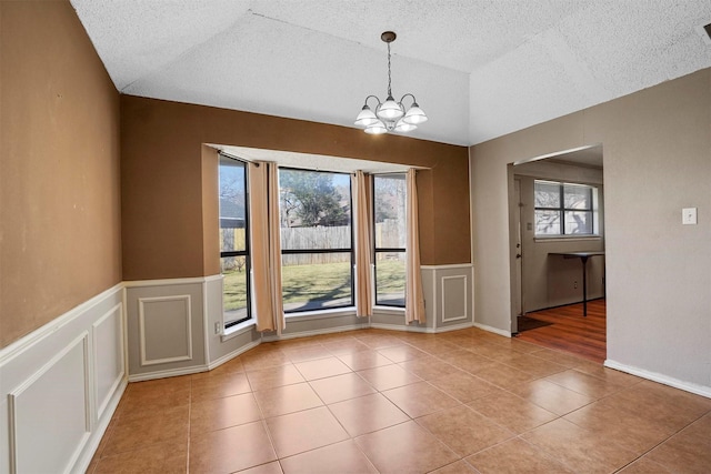 unfurnished dining area featuring lofted ceiling, light tile patterned floors, a decorative wall, and an inviting chandelier