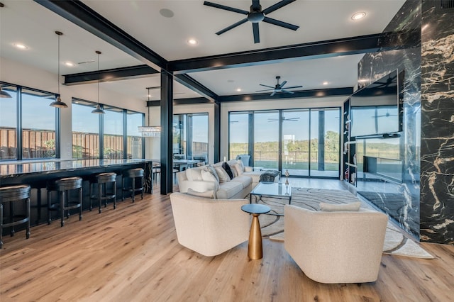 living area with a ceiling fan, wood finished floors, beam ceiling, and a healthy amount of sunlight