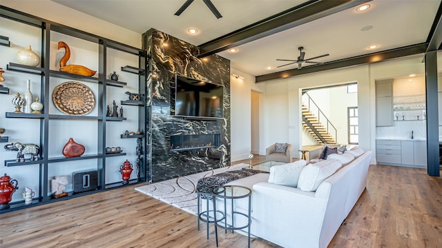 living room featuring a ceiling fan, beamed ceiling, wood finished floors, stairs, and a high end fireplace