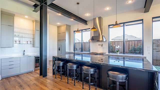 kitchen featuring wall chimney exhaust hood, wine cooler, light wood-style flooring, modern cabinets, and beam ceiling