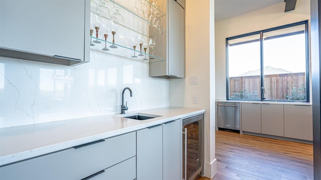 kitchen with beverage cooler, dishwasher, light wood-style flooring, a sink, and backsplash