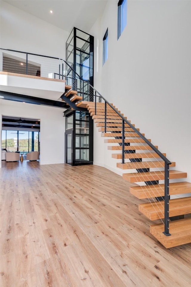 stairway featuring recessed lighting, a high ceiling, and wood finished floors