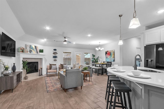 living room featuring ceiling fan with notable chandelier, a fireplace with flush hearth, light wood-style flooring, and recessed lighting