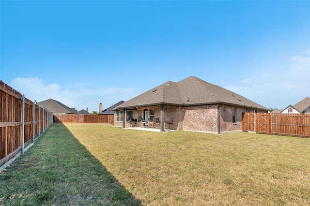 rear view of house featuring brick siding, a patio, a shingled roof, a lawn, and a fenced backyard