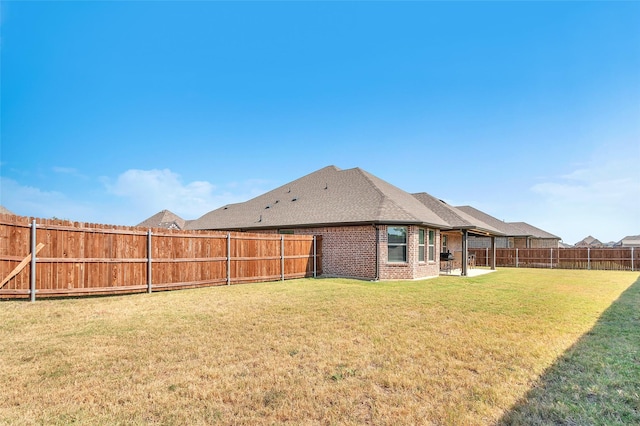 back of house with a shingled roof, a patio, a fenced backyard, a yard, and brick siding