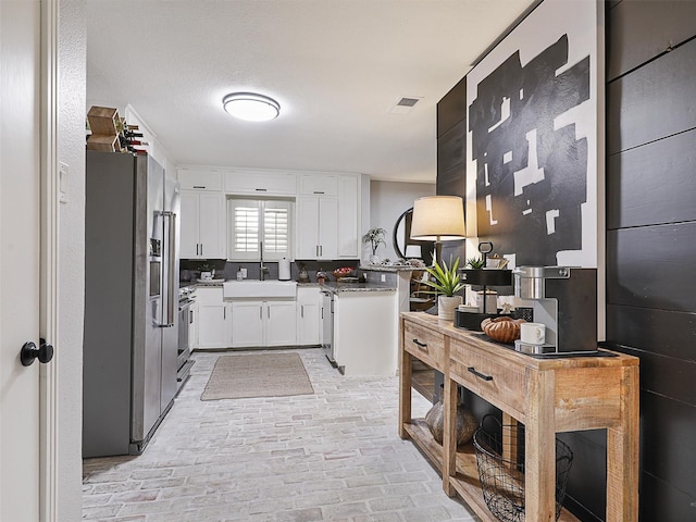 kitchen with brick floor, stainless steel appliances, a sink, visible vents, and white cabinetry