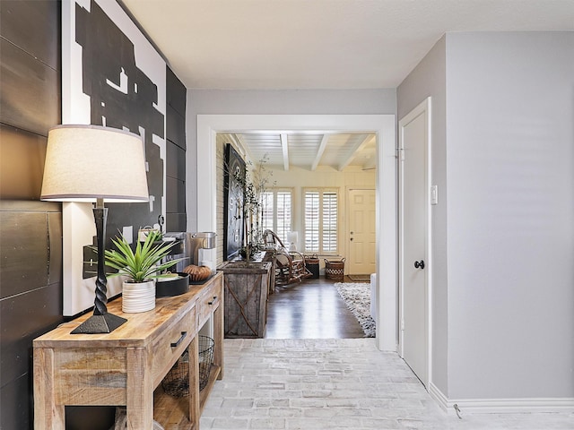 hall featuring brick floor, beamed ceiling, and baseboards