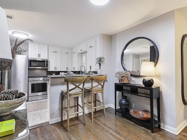 kitchen with stainless steel appliances, a peninsula, dark wood-style flooring, white cabinets, and decorative backsplash