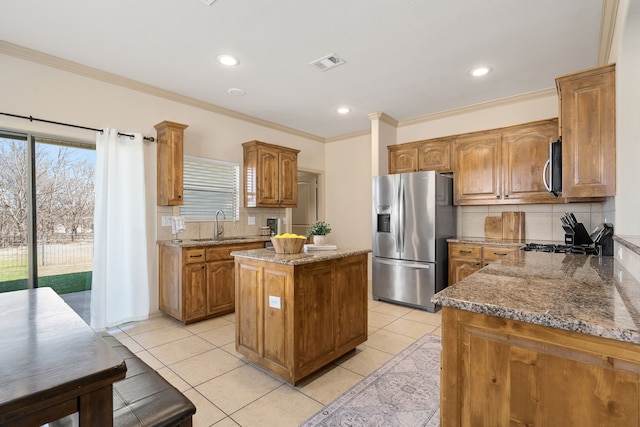 kitchen with stainless steel appliances, a kitchen island, a sink, visible vents, and light stone countertops