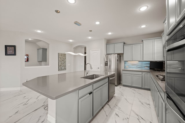 kitchen featuring an island with sink, gray cabinets, marble finish floor, stainless steel appliances, and a sink