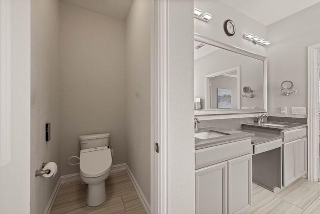 bathroom with vanity, wood finished floors, visible vents, baseboards, and toilet