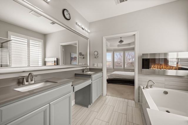 bathroom featuring visible vents, a bathtub, a glass covered fireplace, vanity, and a raised ceiling