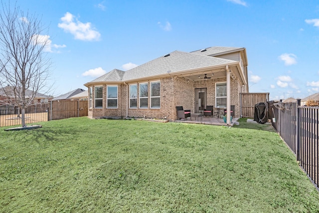 rear view of property with a ceiling fan, a fenced backyard, a yard, brick siding, and a patio area