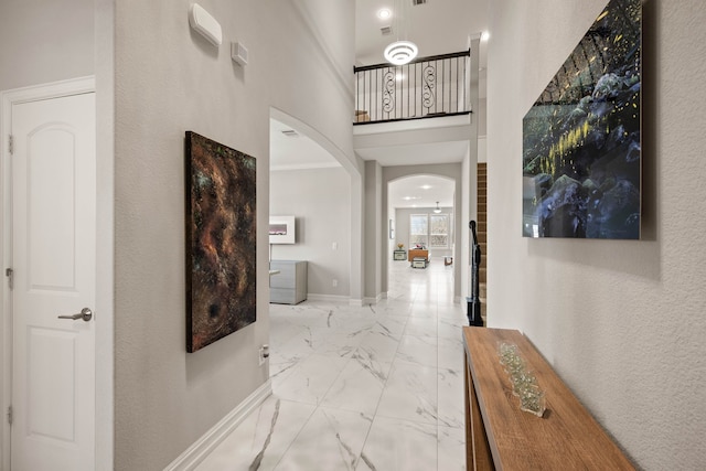 corridor with baseboards, arched walkways, a high ceiling, and marble finish floor