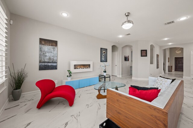 living area featuring arched walkways, visible vents, marble finish floor, and a lit fireplace