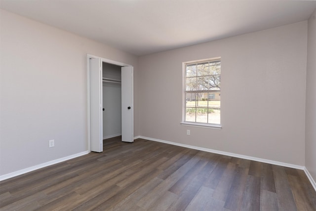 unfurnished bedroom featuring dark wood finished floors, baseboards, and a closet