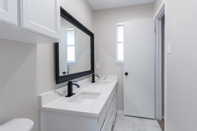 bathroom with a sink, toilet, marble finish floor, and double vanity