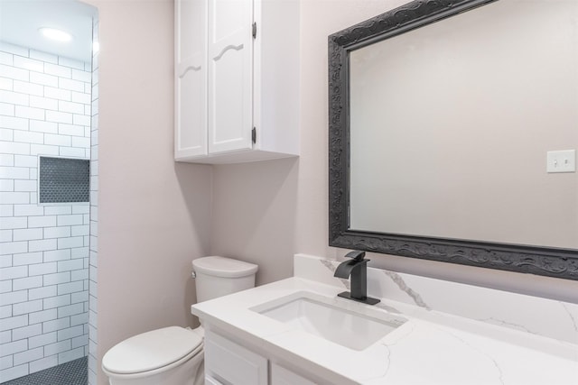 bathroom featuring tiled shower, toilet, and vanity