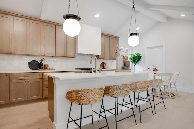 kitchen with decorative backsplash, vaulted ceiling with beams, a kitchen island with sink, light countertops, and a kitchen bar