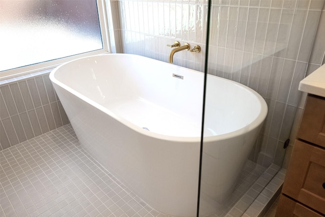 bathroom with a soaking tub, vanity, tile walls, and tile patterned floors