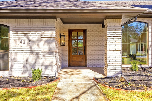 entrance to property featuring brick siding and a shingled roof